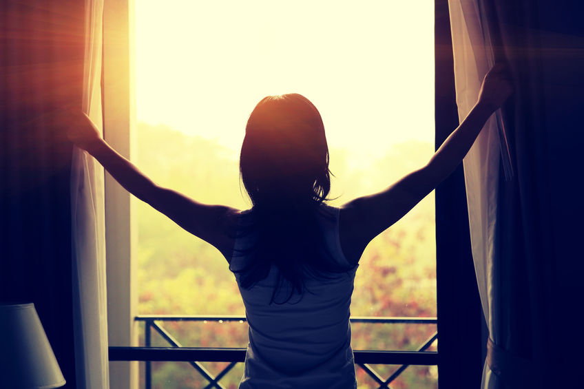 young woman opening curtains in a bedroom
